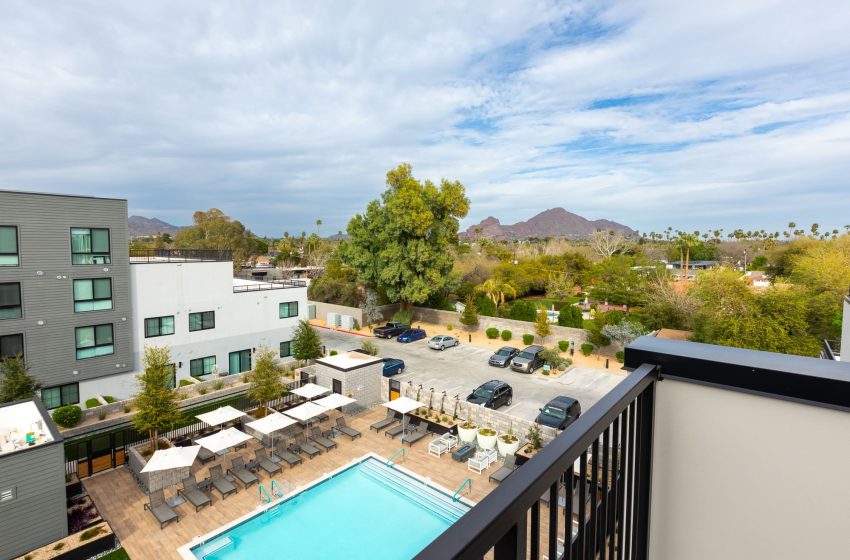 View from a balcony overlooking a residential area with a swimming pool, parking lot, and distant mountains under a cloudy sky.