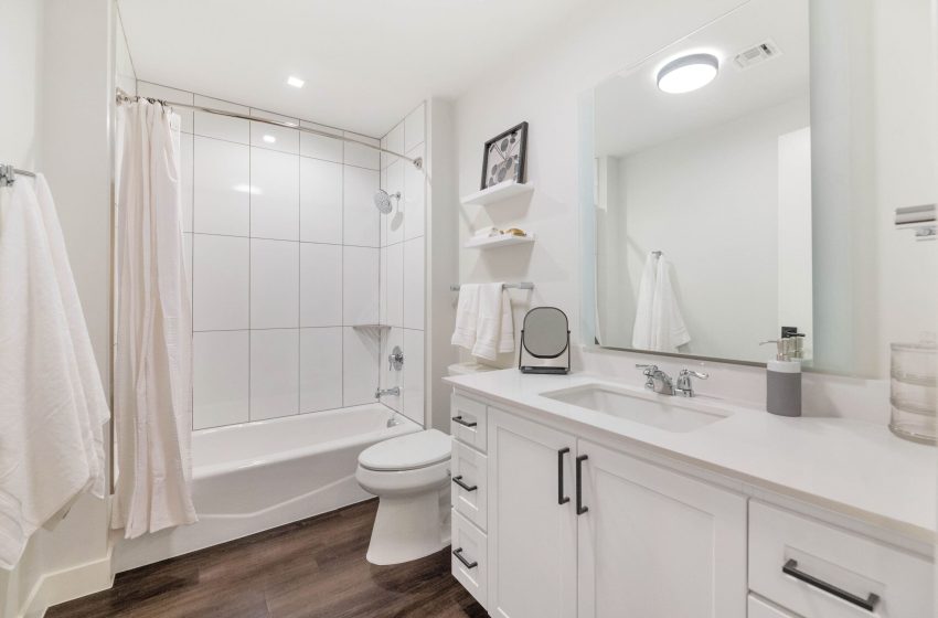 Modern bathroom interior featuring a white vanity with sink, a mirrored cabinet, a toilet, and a bathtub with a shower curtain. towels hang neatly beside the shower.
