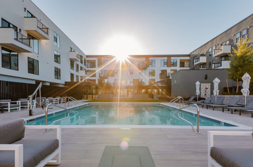 Sunset over a modern apartment complex pool, flanked by loungers and sculptures, with buildings on either side.