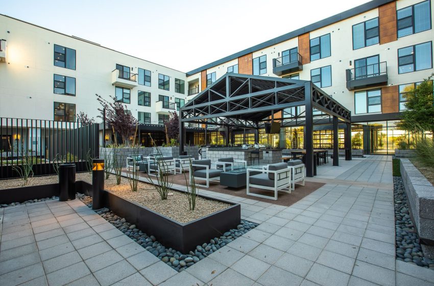 Modern residential courtyard with seating areas, geometric landscaping, a gazebo, and contemporary apartment buildings surrounding the space.